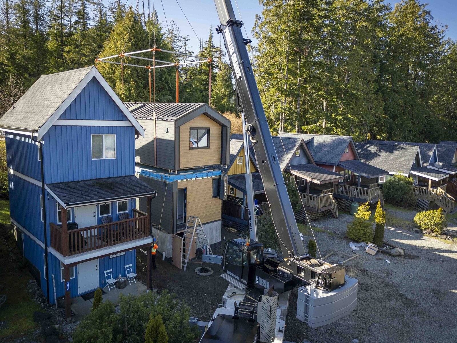 Crane setting a module between houses on a residential street